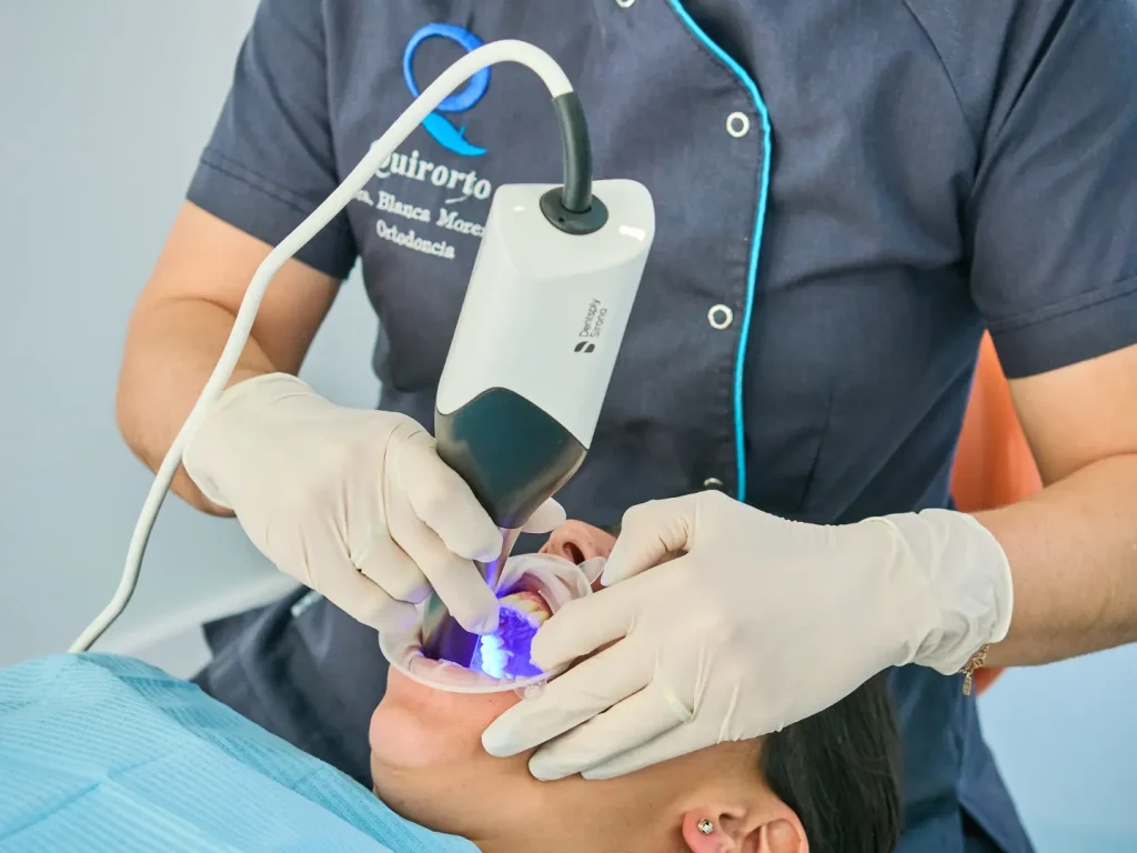 Dentista realizando un escaneo intraoral digital a un paciente con un escáner Dentsply Sirona, utilizando un retractor labial y luz visible del dispositivo.