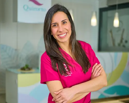 Primer plano de la Dra. Cristina García, directora de la clínica Quiroorto, sonriendo con uniforme fucsia y brazos cruzados en el interior de la clínica.