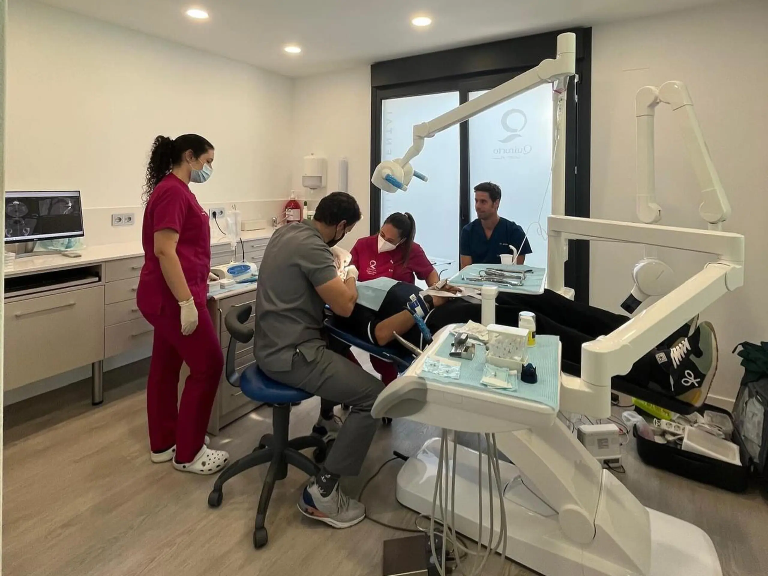 Escena de un consultorio dental moderno con tres profesionales dentales y un paciente recibiendo tratamiento.