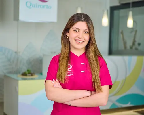 Primer plano de una joven profesional de la clínica Quiroorto, con uniforme fucsia y brackets, posando con los brazos cruzados y sonriendo.
