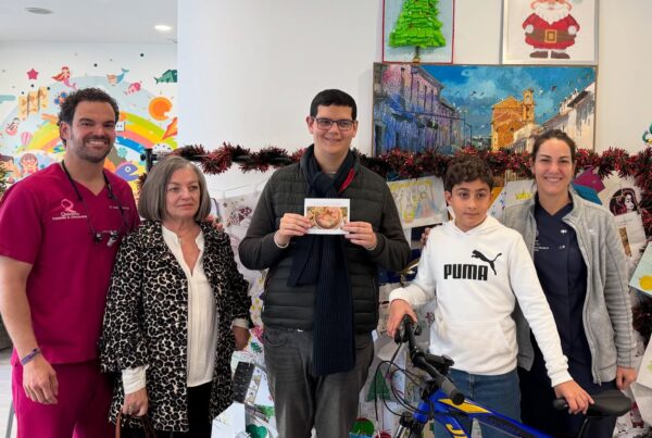 Cinco personas (dos miembros del personal de Quiroorto y tres pacientes/familiares, incluyendo un niño con una bicicleta) posando en la clínica durante la temporada navideña, con un árbol y un cartel de Santa Claus.