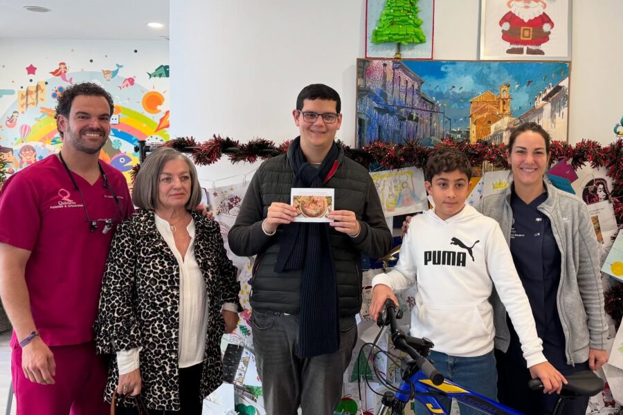 Cinco personas (dos miembros del personal de Quiroorto y tres pacientes/familiares, incluyendo un niño con una bicicleta) posando en la clínica durante la temporada navideña, con un árbol y un cartel de Santa Claus.