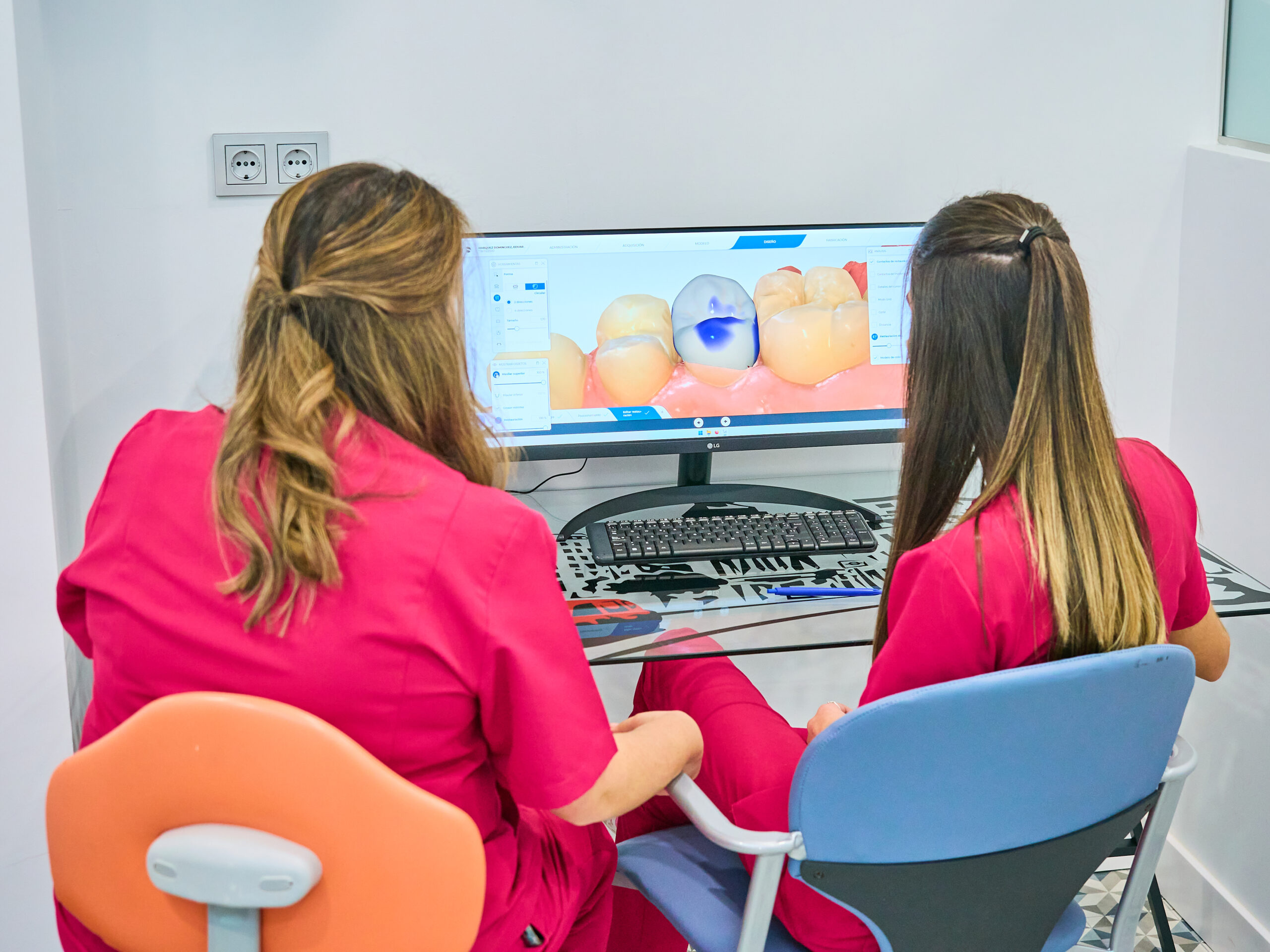 Dos profesionales dentales de espaldas, revisando en un monitor un diseño digital CAD de una corona o incrustación dental.