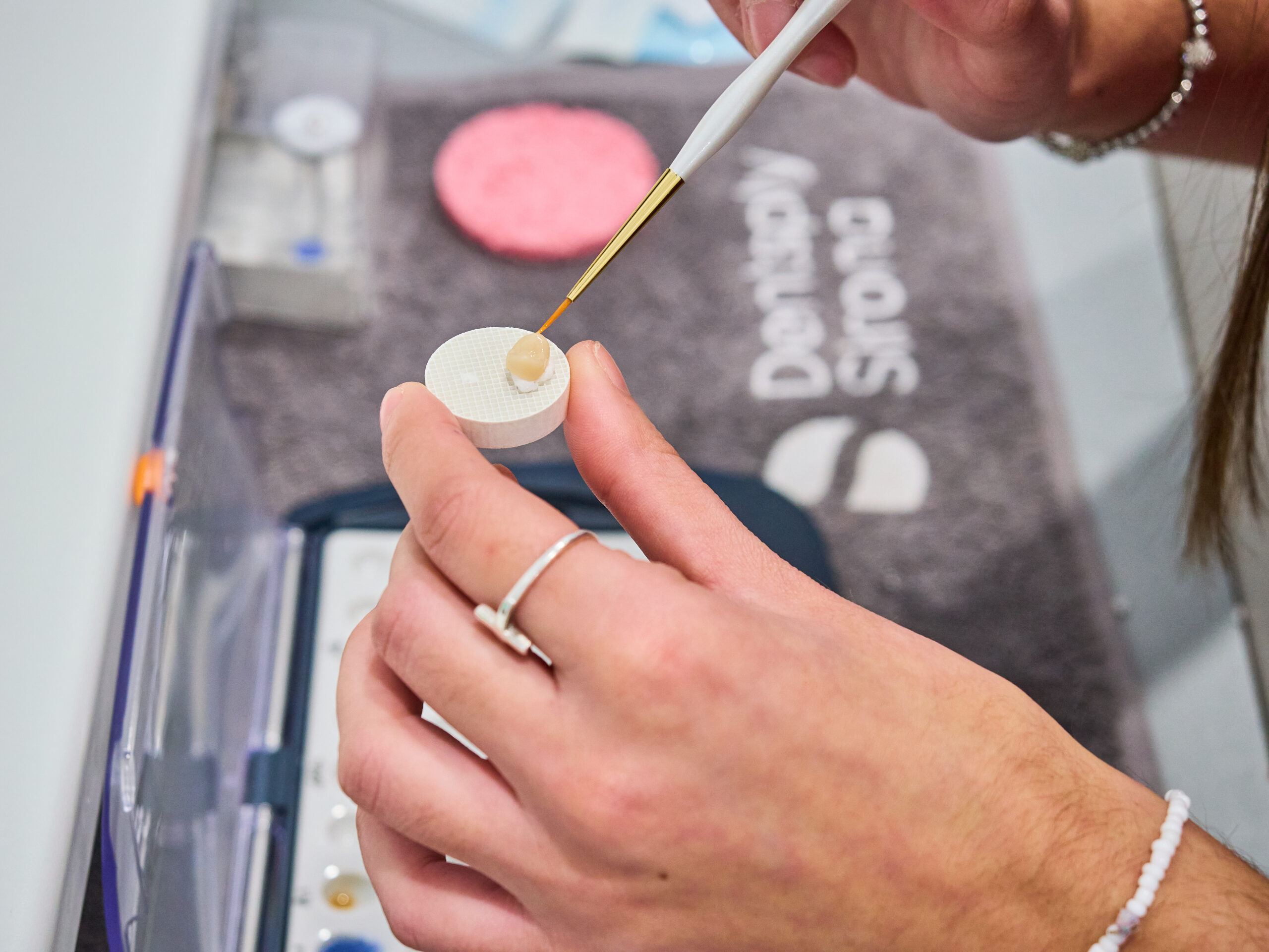 Manos aplicando resina o tintes con un pincel fino a una restauración dental de cerámica o resina.