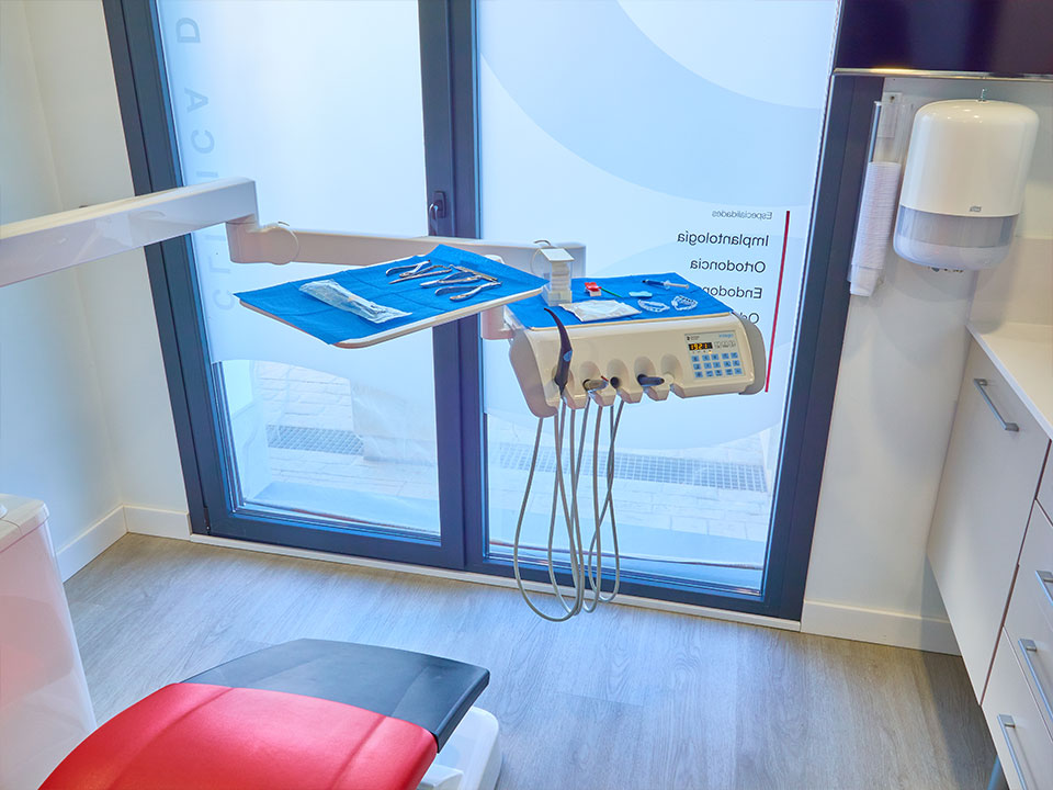 Equipamiento y herramientas dentales quirúrgicas preparadas en la bandeja articulada de una unidad dental frente a una ventana, en una clínica moderna.