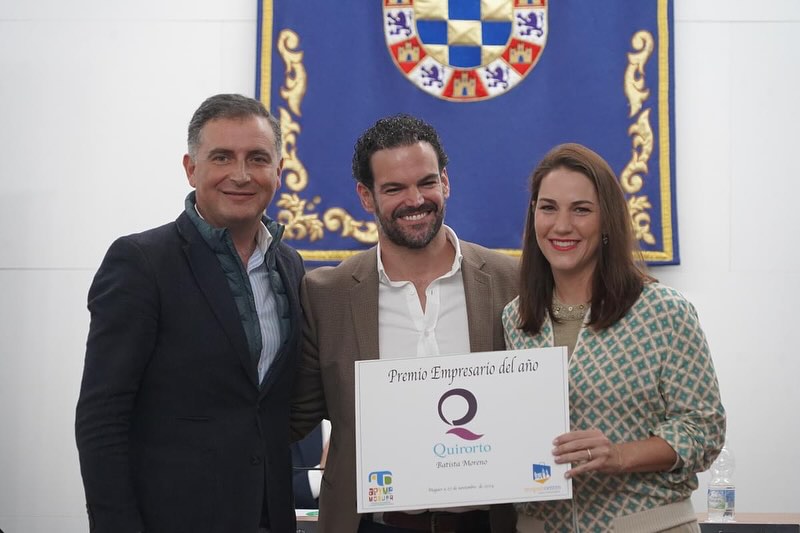 Tres personas (dos hombres y una mujer) posan sonriendo mientras sostienen el certificado del "Premio Empresario del Año" otorgado a Quirorto Batista Moreno, con un escudo institucional de fondo azul.