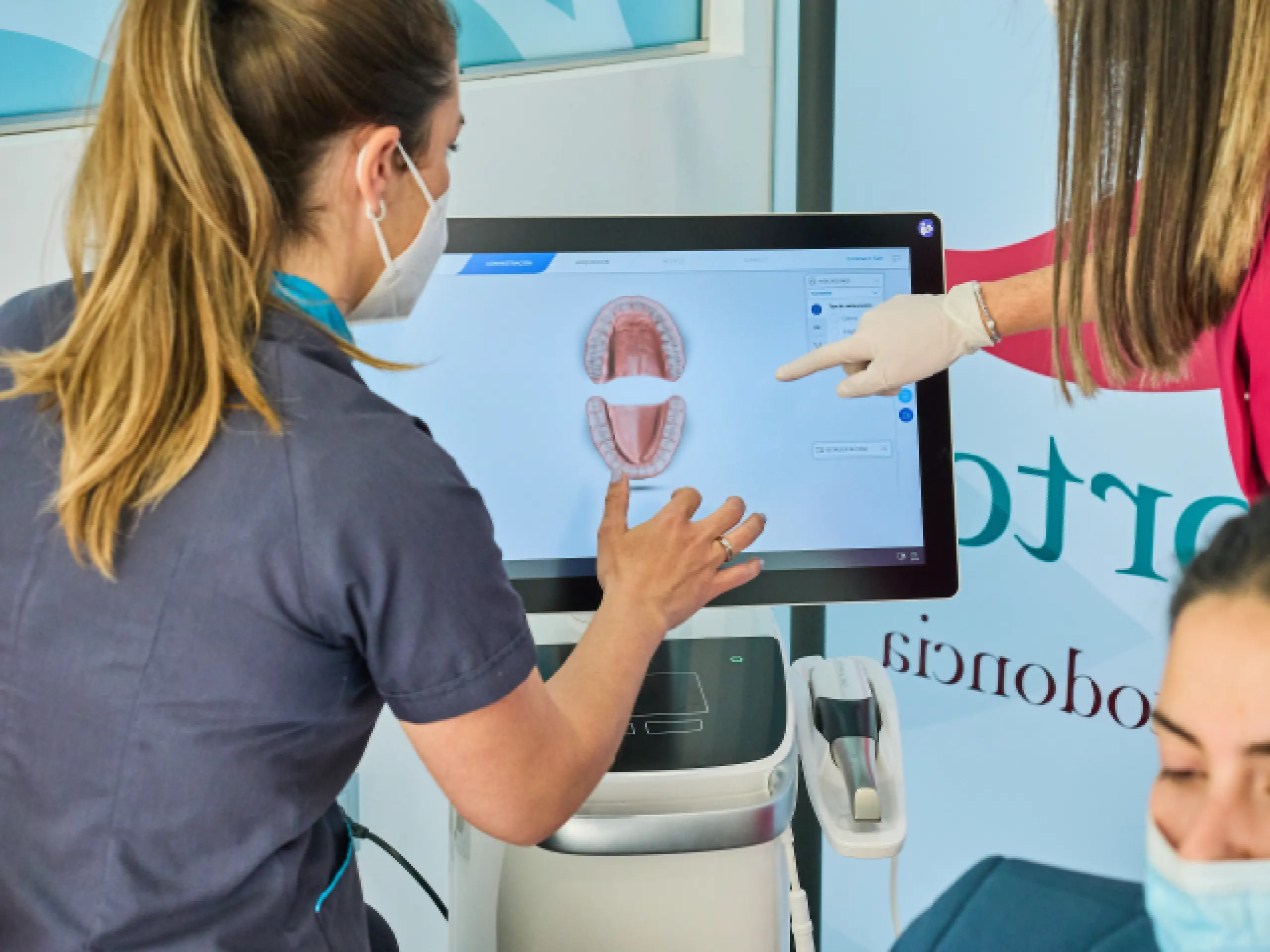 Dos profesionales dentales examinando un modelo digital de la mandíbula y los dientes de un paciente en una pantalla táctil.