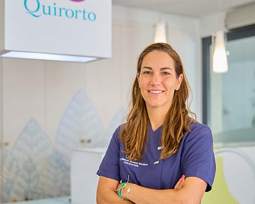 etrato de plano medio de una dentista u ortodoncista con uniforme azul marino, sonriendo con los brazos cruzados, en la recepción de la Clínica Quirorto.