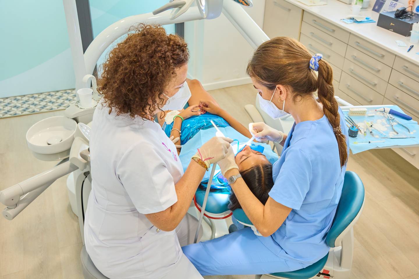 Vista superior de dos odontólogas o asistentes tratando a una paciente en una silla dental.