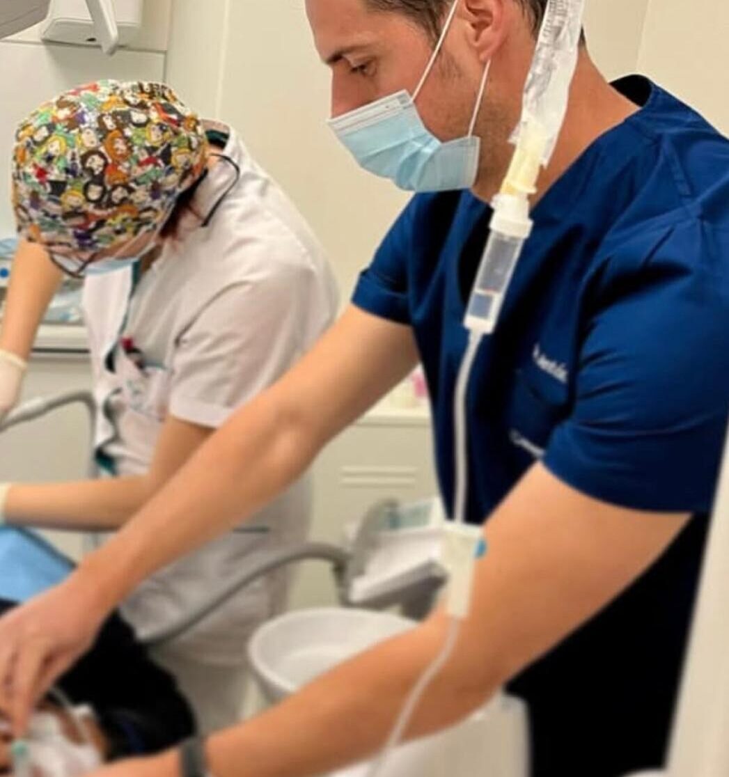 Dos profesionales de la salud, uno con uniforme azul y suero intravenoso, realizando un procedimiento clínico.